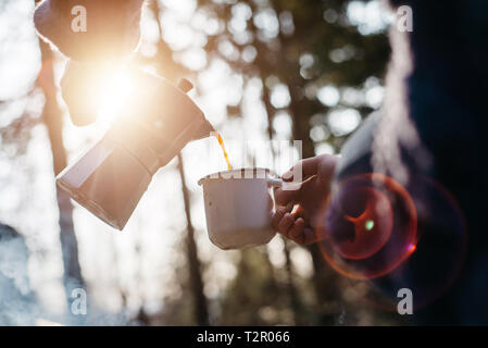 Tourné en plein air de jeune femme verse lui-même boisson chaude dans les montagnes près de feu pendant le coucher du soleil. Traveler fille assise et tenant une tasse de café Banque D'Images