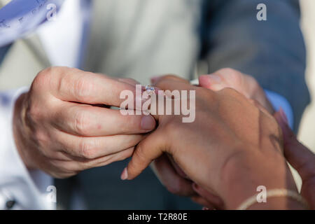 Groom mettant un anneau de mariage par correspondance sur le doigt. Les mariages mixtes - Caucasian man et woman. Banque D'Images