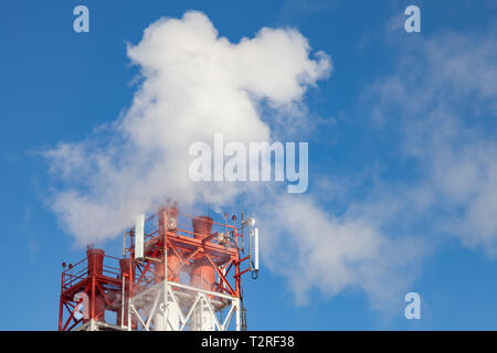 White fumée nocive provenant de la croix rouge et blanc avec des tuyaux d'antennes de communication mobile dans une usine dans le centre-ville dans le contexte de Banque D'Images