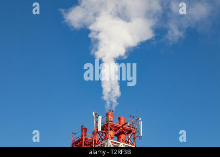 White fumée nocive provenant de la croix rouge et blanc avec des tuyaux d'antennes de communication mobile dans une usine dans le centre-ville dans le contexte de Banque D'Images