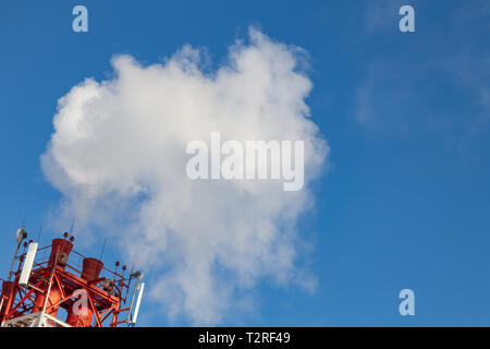 White fumée nocive provenant de la croix rouge et blanc avec des tuyaux d'antennes de communication mobile dans une usine dans le centre-ville dans le contexte de Banque D'Images