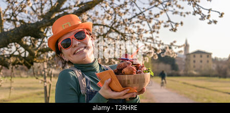 Happy woman in hat orange et verres pour la maison de la fête du Roi des Pays-Bas, tenant un bol avec des beignes. Des pâtisseries traditionnelles pour le festival Banque D'Images