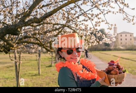 Happy woman in hat orange et verres pour la maison de la fête du Roi des Pays-Bas, tenant un bol avec des beignes. Des pâtisseries traditionnelles pour le festival Banque D'Images