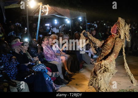 JANJANBUREH, la Gambie (19/01/2019) - Les touristes étrangers regardez une Ifangbondi Kankurang exécuter pendant l'Janjanbureh Kankurang Festival. Le Festival Janjanbureh Kankurang fait partie d'efforts conjoints de l'UE au Fonds d'affectation spéciale d'urgence pour l'Afrique et le projet d'autonomisation des jeunes Gambiens pour stimuler le tourisme à Janjanbureh. En préservant et en célébrant le patrimoine culturel de l'Kankurang, c'est la création de nouvelles possibilités économiques pour les jeunes Gambiens sous la forme d'une augmentation du tourisme. Banque D'Images