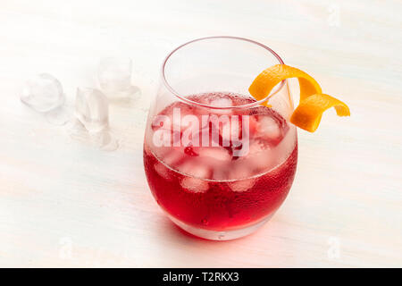 Un cocktail Negroni dynamique avec un zeste d'orange et campari twist, avec des cubes de glace sur un fond en bois blanc, avec copie espace Banque D'Images