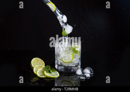 Plage d'été Mojito cocktail tropical rafraîchissant dans le verre avec l'eau gazeuse, jus de lime, les feuilles de menthe, sucre, rhum et glace réfléchissante sur surf noir Banque D'Images