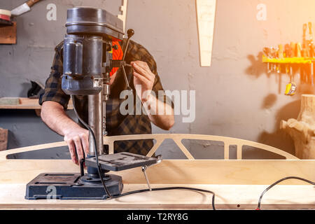 Portrait d'un homme avec des vêtements de travail et d'une menuiserie cap est une sculpture de bois sur une grande machine de forage modernes dans un atelier de la lumière. Accueil repa Banque D'Images