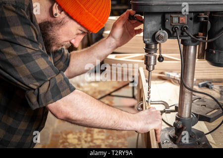 Portrait d'un homme avec des vêtements de travail et d'une menuiserie cap est une sculpture de bois sur une grande machine de forage modernes dans un atelier de la lumière. Accueil repa Banque D'Images