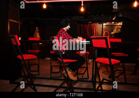 L'homme indien en chemise à carreaux et turban noir, assis au bar. Banque D'Images