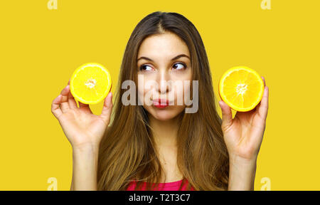 Closeup portrait confus, troublé, malheureux, young woman holding, fille, deux demi-orange, incertaine pour le manger. Visage humain expressions, emoti Banque D'Images