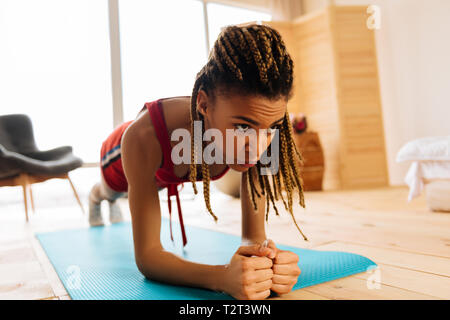 Plank épuisante. Femme aux yeux noirs avec de belles tresses sentiment épuisé tout en terminant l'entraînement avec plank Banque D'Images