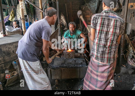 3 Les hommes qui travaillent dans l'atelier de forgeron à Dhaka, au Bangladesh. 1 man with mobile phone dans l'arrière-plan. Banque D'Images