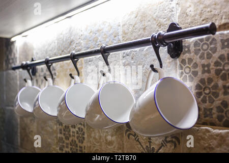 Tasses blanc céramique accroché sur des crochets dans la cuisine Banque D'Images