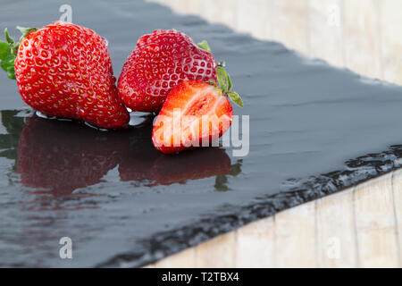 Close-up de trois fraises isolé sur une plaque en ardoise carré mouillé sur un fond blanc tourné en high angle view with selective focus Banque D'Images