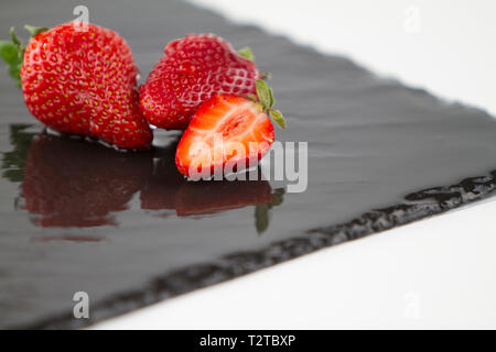 Close-up de trois fraises isolé sur une plaque en ardoise carré mouillé sur un fond blanc tourné en high angle view with selective focus Banque D'Images