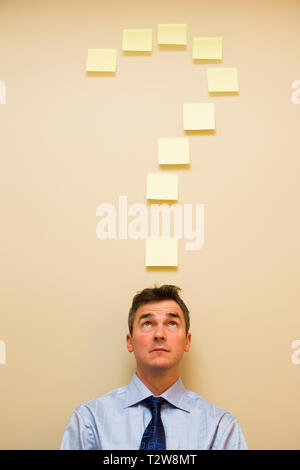 Caucasian middle aged businessman sous post it en forme de point d'interrogation Banque D'Images