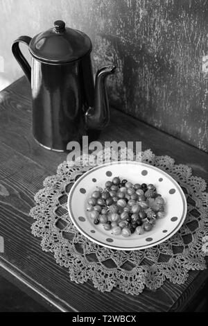 Vintage coffee pot émaillé et l'assiette de fruits de jardin sur la serviette décorative en bonneterie. Nature morte noir et blanc Banque D'Images