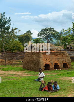 Les enfants se coucher sur le sol en face d'un petit four en briques dans un village du Malawi Banque D'Images