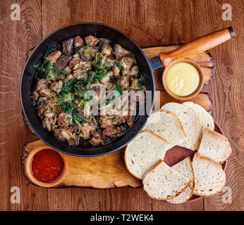 Tranches de viande dans une poêle avec le foie, le cœur et les oignons. Sauce blanche et rouge et du pain avec poêle avec la viande. À partir de la photo ci-dessus Banque D'Images