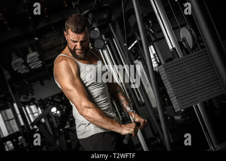 Bodybuilder barbu à l'exercice permanent de sport faisant câble déroulant bras avec effort de serrer les dents Banque D'Images