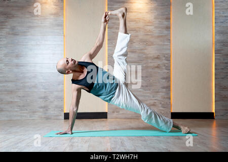 Athletic homme debout sur bras et jambe avec part soulevé vers le haut de faire le yoga sur le tapis de gym bleu. Banque D'Images