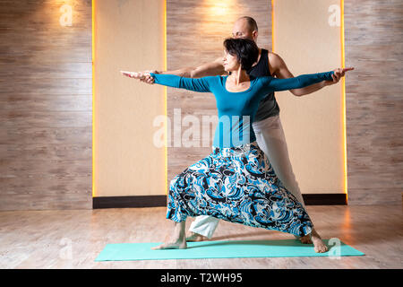 L'homme et la femme sont adultes pratiquant le yoga en se tenant sur le tapis bleu dans la salle de sport. Banque D'Images