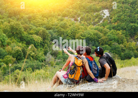 Image de deux hommes et une femme en tenant assis sur selfies colline avec la végétation en après-midi Banque D'Images