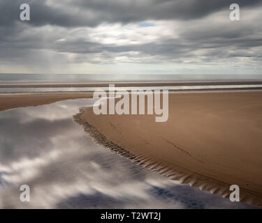 Un petit ruisseau coule vers le bas St Cyrus beach reflétant la motion de nuages dans le ciel au-dessus, dans l'Aberdeenshire, Ecosse, Royaume-Uni Banque D'Images