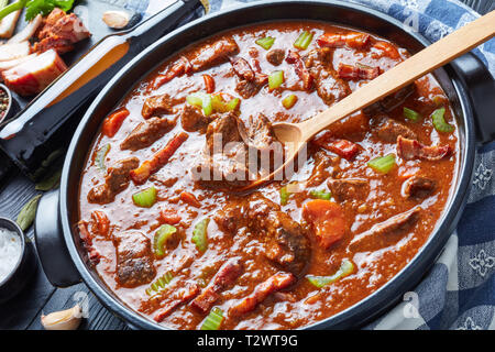 Boeuf et à la bière irlandaise traditionnelle ragoût avec carottes, céleri, carottes et des épices dans une cocotte avec des ingrédients et une bouteille de bière sur un w noir Banque D'Images