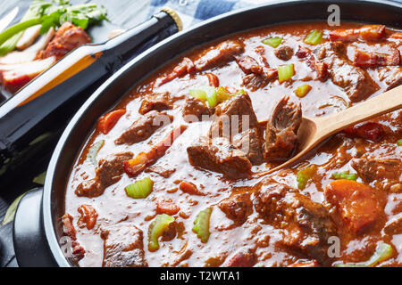 Boeuf irlandais classique et de la bière avec Ragoût de carottes, de bacon, de céleri, les carottes et les épices dans une cocotte avec des ingrédients et une bouteille de bière sur un blac Banque D'Images