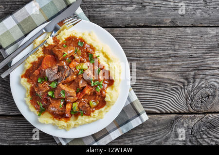 Purée de pommes de terre garni de ragoût de boeuf irlandais sur une assiette avec des couverts, sur une table en bois, vue de dessus, flatlay, copy space Banque D'Images