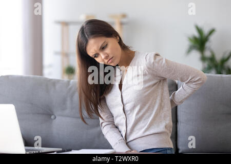 Mauvaise young woman sitting on couch souffre de maux de dos Banque D'Images