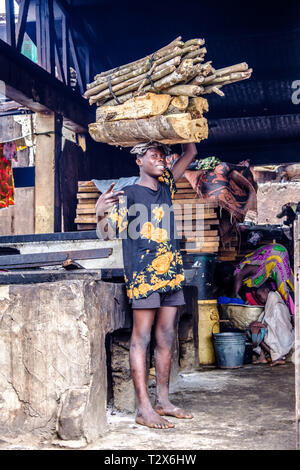 SEKONDI TAKORADI, GHANA - 10 avril 2018 : Jeune homme charge lourde de soldes du bois sur la tête de Bosomtwi Sam Port de pêche, marché aux poissons Banque D'Images