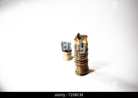 Maisons miniatures sur le dessus des piles de pièces de monnaie pour représenter les différences de prix Banque D'Images