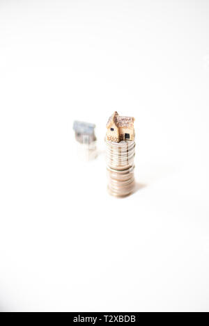 Maisons miniatures sur le dessus des piles de pièces de monnaie pour représenter les différences de prix Banque D'Images