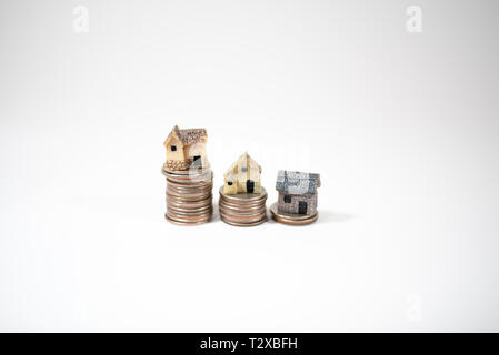 Maisons miniatures sur le dessus des piles de pièces de monnaie pour représenter les différences de prix Banque D'Images
