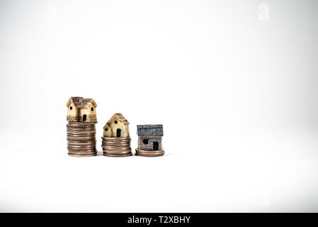 Maisons miniatures sur le dessus des piles de pièces de monnaie pour représenter les différences de prix Banque D'Images