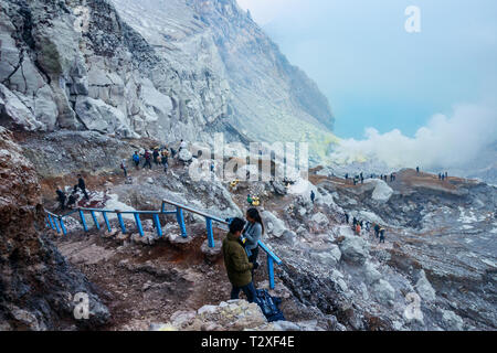 Vue sur le cratère du Kawah Ijen avec les touristes et les mineurs de soufre de grimper la pente et toxiques gaz sulfurique emeging du lac. L'île de Java en Indonésie. Banque D'Images