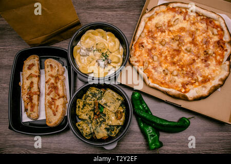 Mise à plat. Boîte de pizza avec poivrons verts, pain à l'ail, fetuccine et ravioli sur la boîte en plastique. Cuisine italienne rapide à la maison Banque D'Images