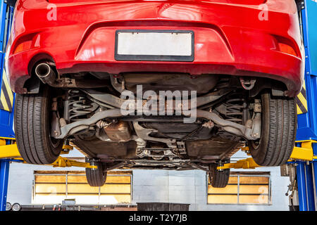 Véhicule rouge levé sur le circuit hydraulique de levage voiture à un atelier au cours de l'entretien courant Banque D'Images