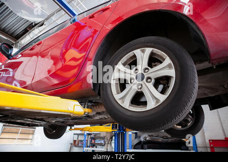 Voiture rouge levé sur le circuit hydraulique de levage voiture à un atelier au cours de l'entretien courant Banque D'Images