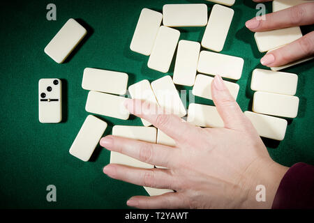 Les mains sur les os domino mélange une table recouverte de tissu vert Banque D'Images