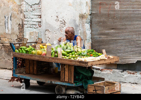 La Havane, Cuba - 25 juillet 2018 : Un homme assis derrière son panier de fruits de fumer une cigarette tout en vendant des fruits sur les rues de La Havane à Cuba. Banque D'Images