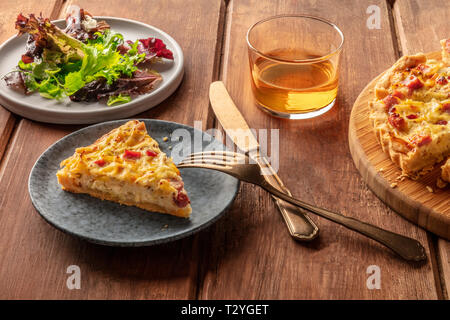 Un dîner français. Une tranche d'une quiche lorraine avec feuilles de mesclun et vin blanc sur un fond de bois rustique foncé Banque D'Images