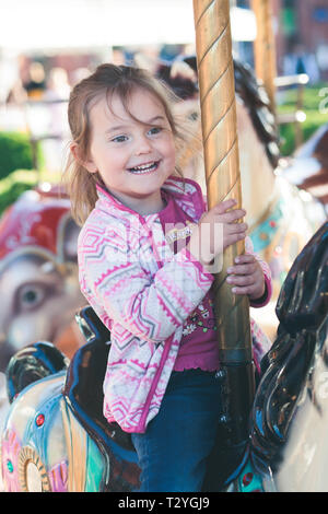 Adorable petit smiling girl riding a horse carousel au rond-point sur la fête foraine Banque D'Images