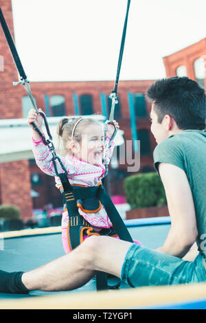 Adorable petit smiling girl jumping on trampoline, s'amusant avec son frère à la fête foraine Banque D'Images