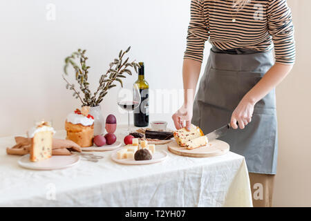 Couper le gâteau de Pâques dans la main de femme. Pâques orthodoxe traditionnelle du pain sucré, kulich. Vacances de Pâques petit déjeuner. Gâteau de Pâques coupe féminine. Banque D'Images