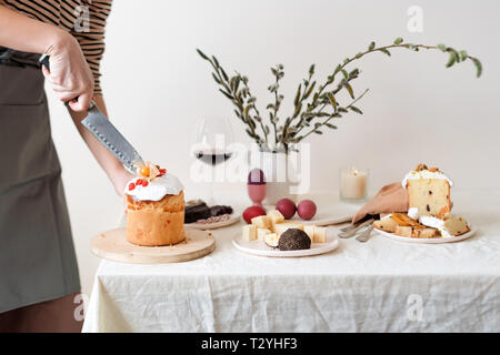 Couper le gâteau de Pâques dans la main de femme. Pâques orthodoxe traditionnelle du pain sucré, kulich. Vacances de Pâques petit déjeuner. Gâteau de Pâques coupe féminine. Banque D'Images