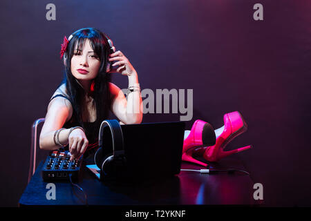 Jeune DJ femme vêtue de chaussures rose aime la musique. Glamorous girl avec headphne sur fond rouge et bleu joue une musique disko. Banque D'Images