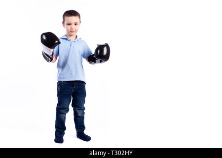 Un petit garçon aux cheveux noirs en jeans, un polo bleu en noir et blanc des gants de boxe s'amuse, montrant des biceps et se considérant un Banque D'Images